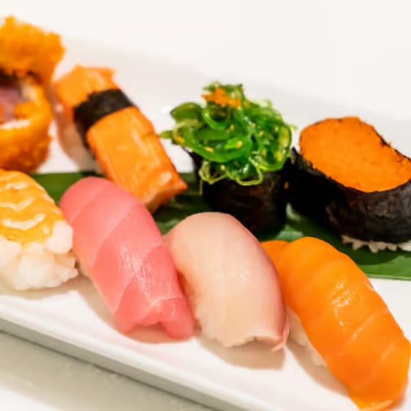 A white plate displays various colorful sushi pieces, including nigiri, gunkan maki, and a sushi roll.