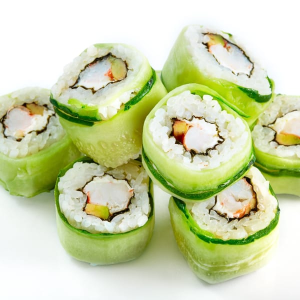 Several cucumber-wrapped sushi rolls with rice, crab, and avocado filling on a white background.