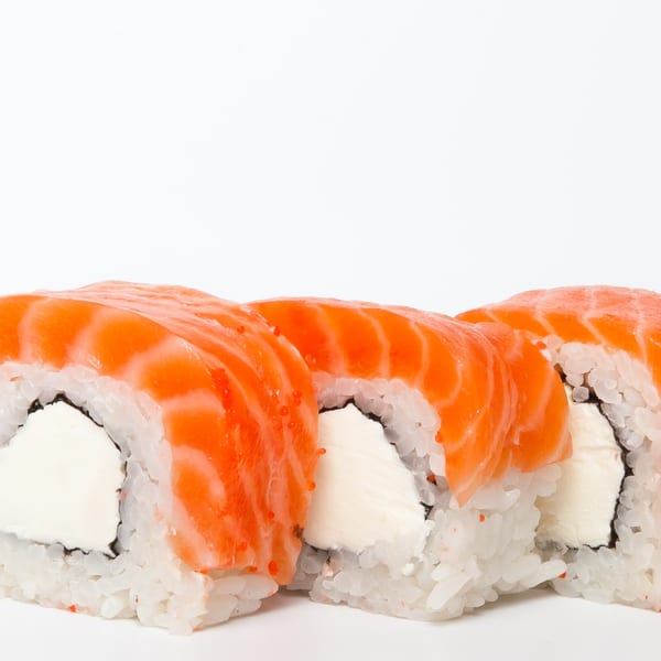 Three salmon sushi rolls with cream cheese filling and rice, on a white background.