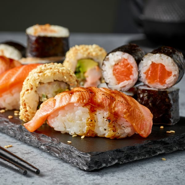 Assorted sushi rolls and nigiri with salmon and sesame seeds on a dark slate board.